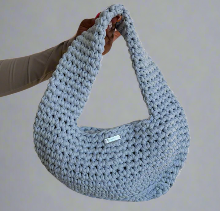 Blue crochet bag held by a person against a white background