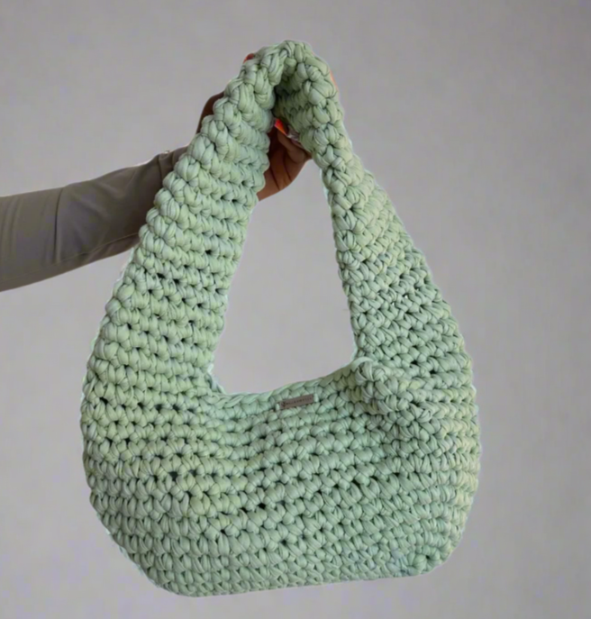 Green knitted bag held by a person against a white background